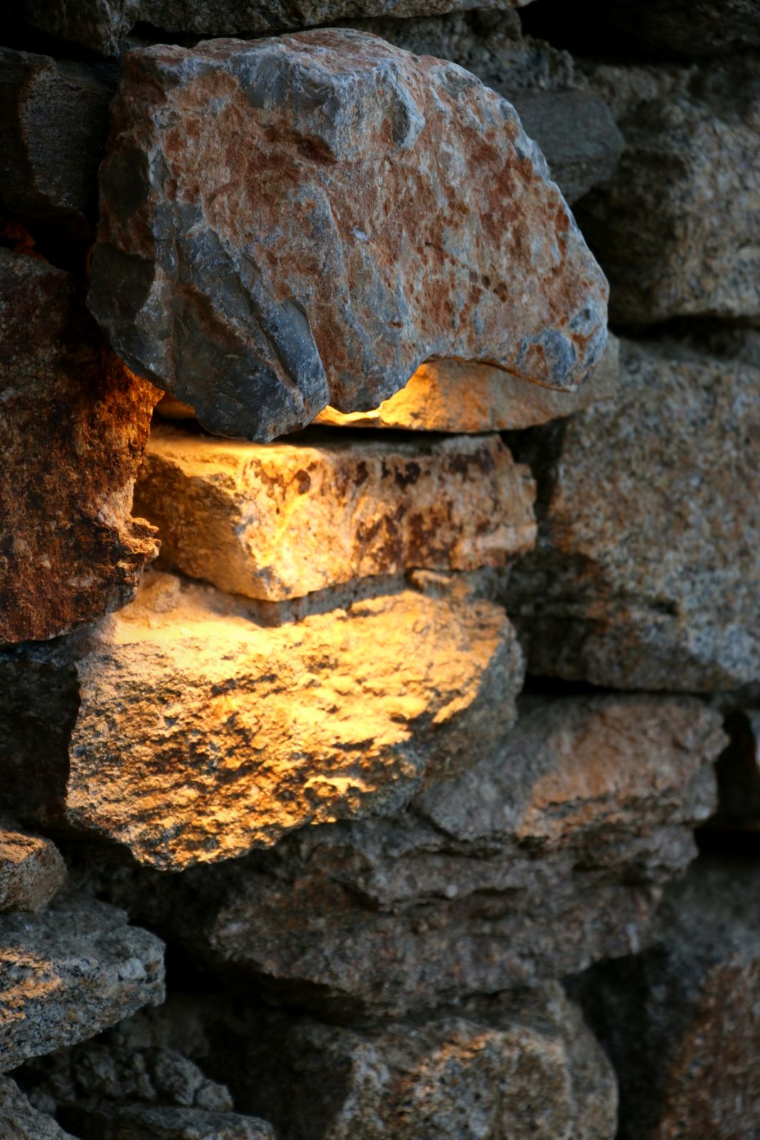A dry stone wall at Alemàgou seen close, one rock lit warm from a source hidden beneath it.