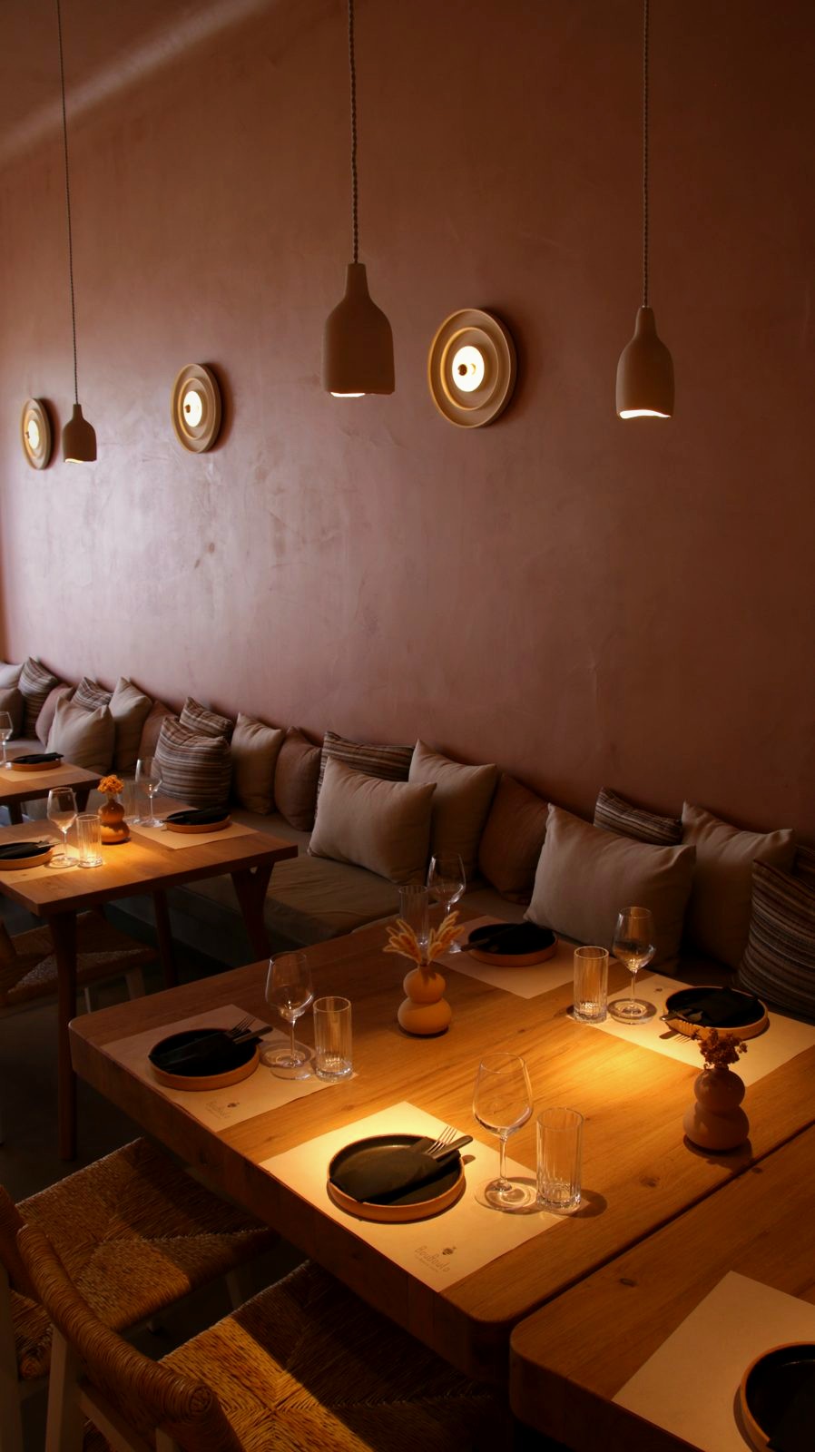 The Bouboulo dining room: cone pendants over timber tables, round sconces on clay colored walls and a cushioned banquette.