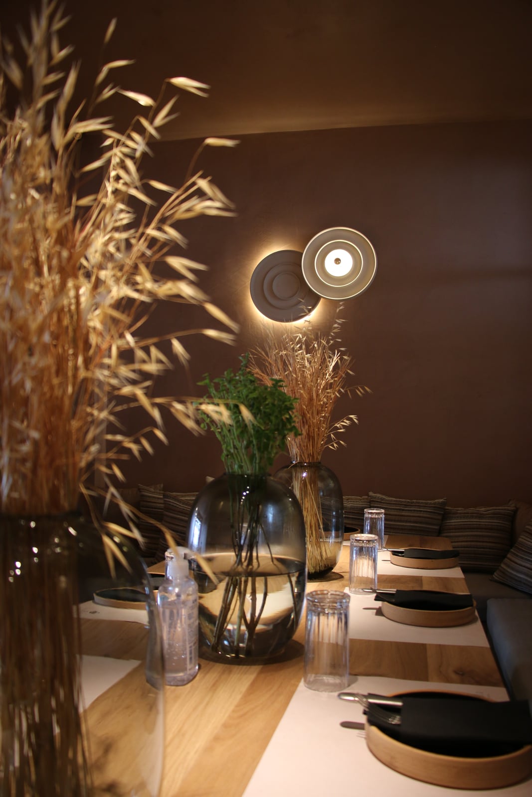 Dried grasses and glass vases on a set table at Bouboulo, a round sconce glowing on the wall behind.