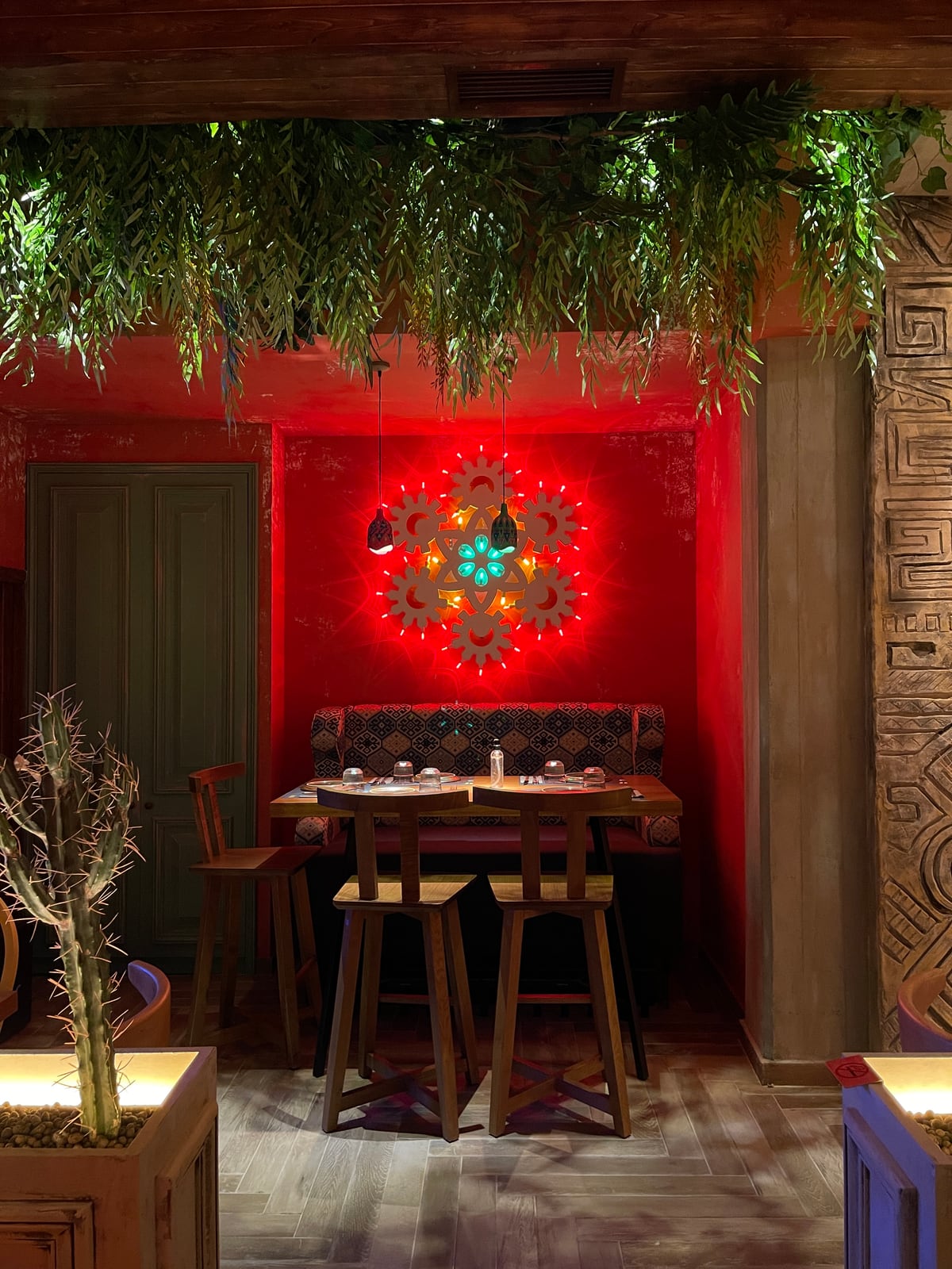 Hanging planting over a red alcove at Panchito, its cut out pattern glowing behind high stools, a cactus in the foreground.