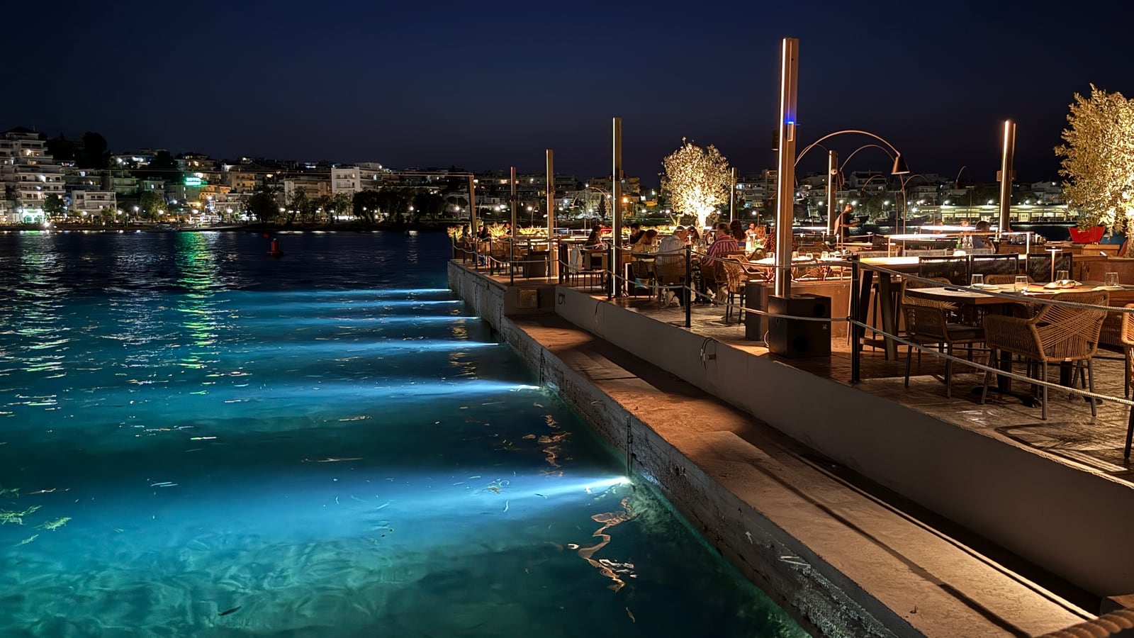 At night the sea below the Raval quay glows turquoise under lights set in its edge, the tables lit along the water and the town across the bay.